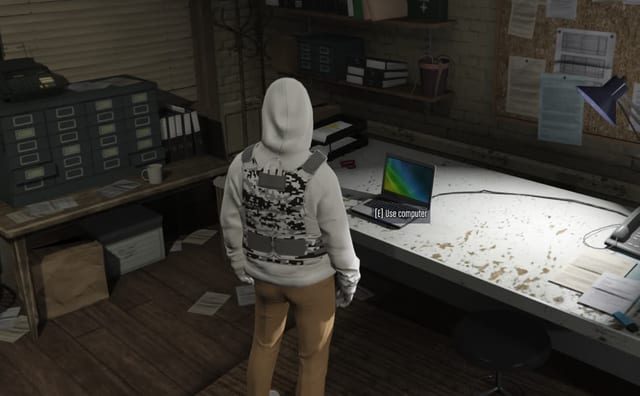 Player in a cluttered office looking at a laptop with the prompt "[E] Use computer".