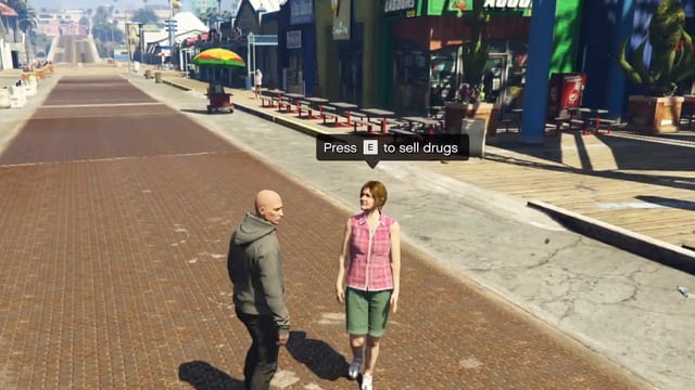Player in a grey hoodie and a woman in a pink checked shirt facing each other on a brick walkway beside shops and picnic tables, with the prompt "Press E to sell drugs" above them.
