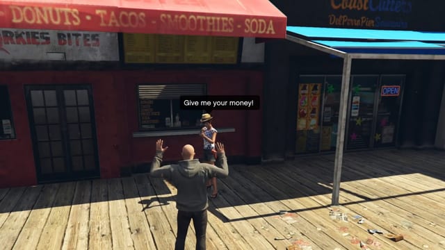 Player with raised hands in front of a woman in a straw hat under the speech bubble "Give me your money!", outside a snack kiosk on a wooden pier.