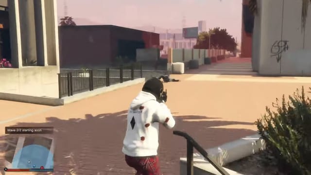 Player in a white hoodie aiming a gun across a paved plaza at a figure lying on the ground, with the notification "Wave 2/2 starting soon" above the minimap.