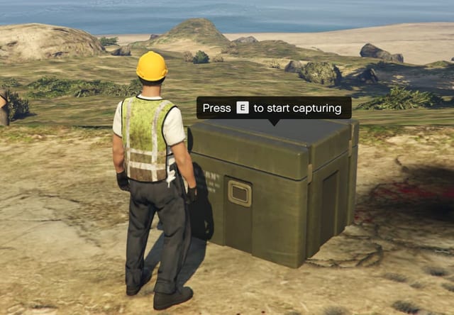 Player in a hi-vis vest beside an army crate with the prompt "Press E to start capturing".