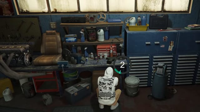 Hooded player crouched at a cluttered workbench in a blue-walled workshop, with a circular countdown showing 2 beside him.