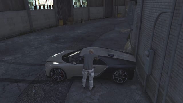 Mechanic leaning into a white and black sports car with a dented front, parked against a brick wall in a dark alley.