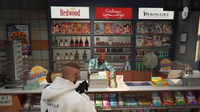 Player in a white hoodie aiming a pistol across a shop counter at a cashier who reaches into the cash register, in front of cigarette and magazine shelves.