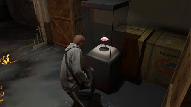 Player with a duffel bag beside a glass display case holding a pink gem on a stand, with wooden crates behind.