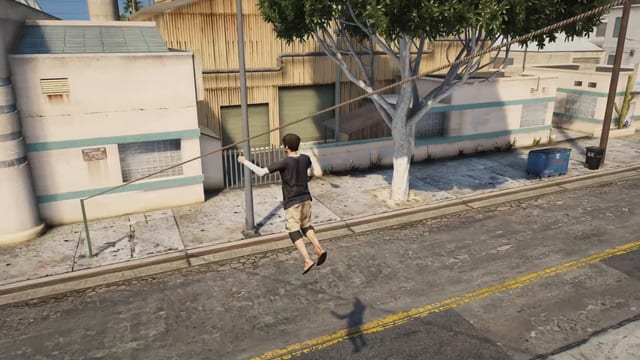 Player hanging by one hand from a rope that runs from above a tree down to a green pole on the pavement, gliding over a street.