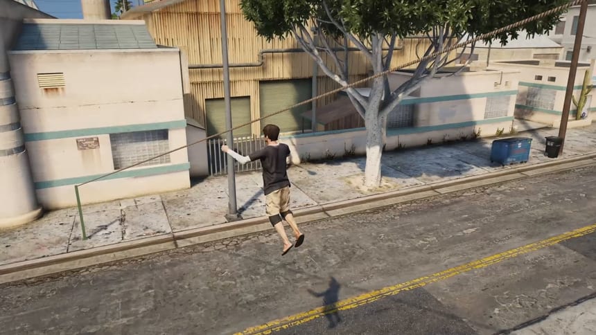 Player hanging by one hand from a rope that runs from above a tree down to a green pole on the pavement, gliding over a street.