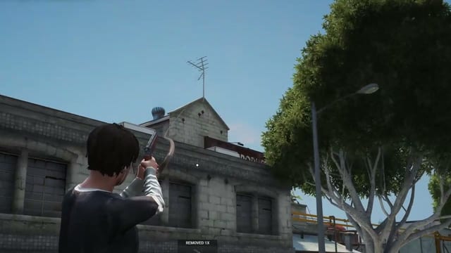 Player aiming a grapple gun upward beside a grey block building and a large tree, with an item notification at the bottom.